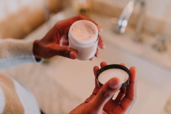 Person Holding a Plastic Container with Cream and a Lid